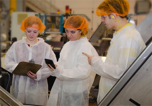 Three students wearing ppe measuring the performance of an assembly line