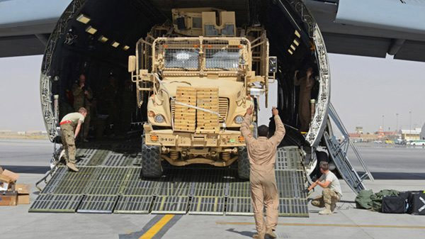 A soldier guiding a truck off of a military transport plane