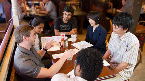 A male alumnus and five operations research students sitting at a restaurant table