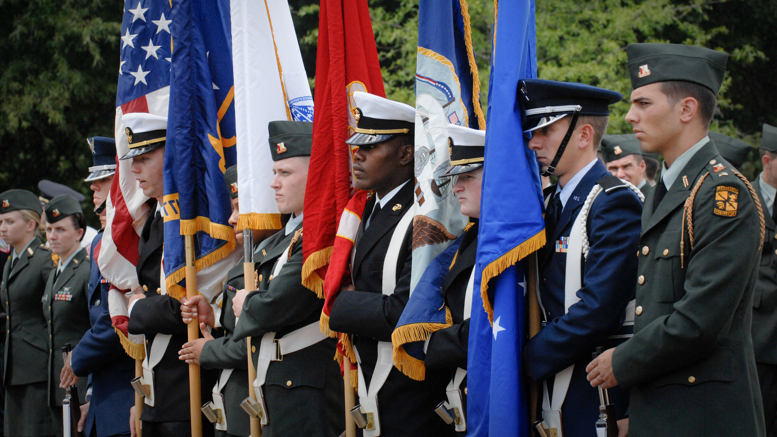 A line of military service members holding flags from the US and all brands of the military