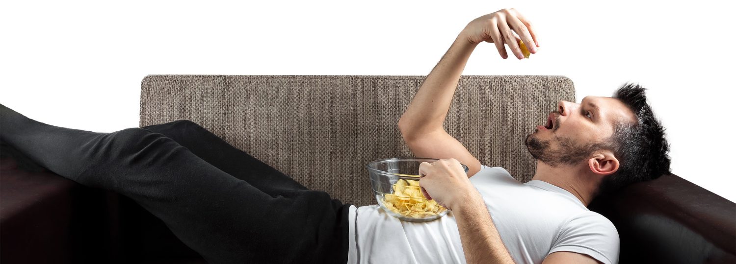 A man laying on a couch eating chips