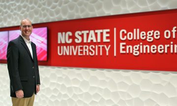 Russ Nelson standing in front of the large NC State University College of Engineering sign in Fitts-Woolard Hall